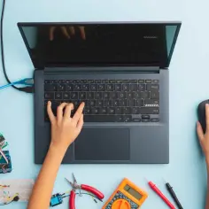 Dziecko uczy się kodowania dla dzieci, pisząc na laptopie. Wokół rozłożone są elementy elektroniczne i narzędzia.