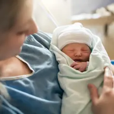 Mama tuli dziecko, które śpi otulone kocykiem. To piękny moment, który może być wspierany przez zasiłek rodzicielski.