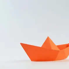 Pomarańczowy papierowy stateczek, klasyczne origami, gotowy do wypłynięcia na przygodę.