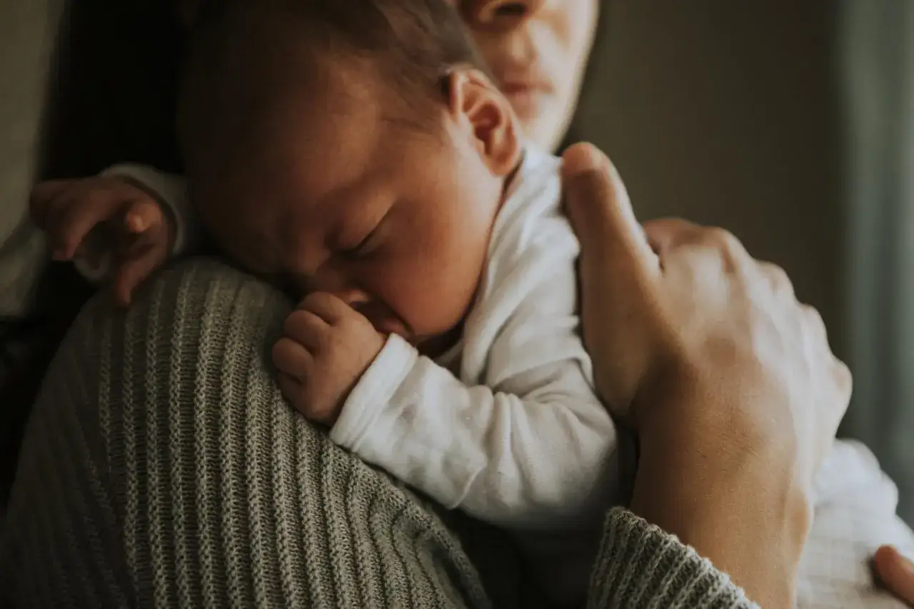 Słodki noworodek śpi wtulony w ramię mamy, otulony ciepłym swetrem.