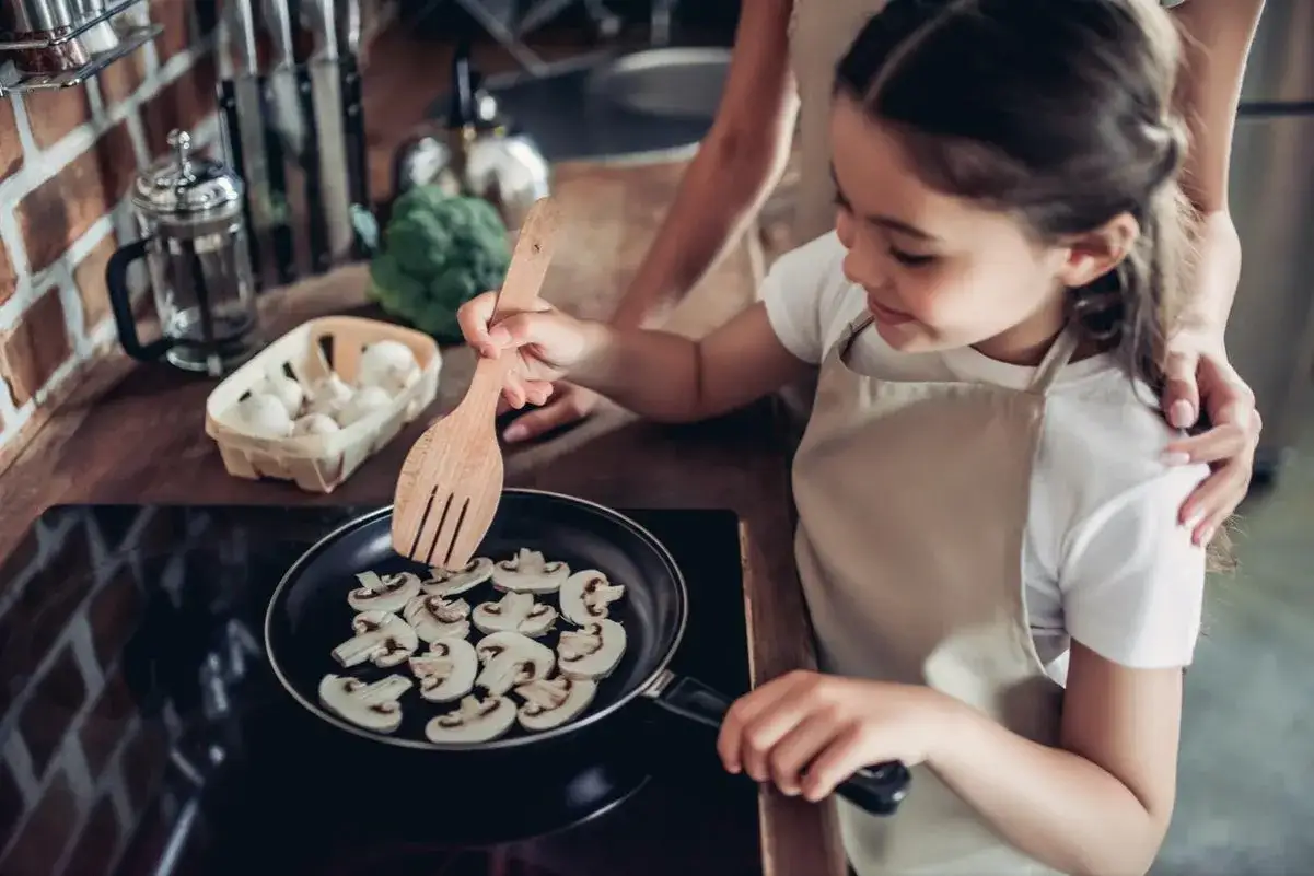 Mała dziewczynka z mamą gotuje pieczarki na patelni. Od kiedy dziecko może jeść pieczarki? Odpowiedź znajdziesz w kuchni!