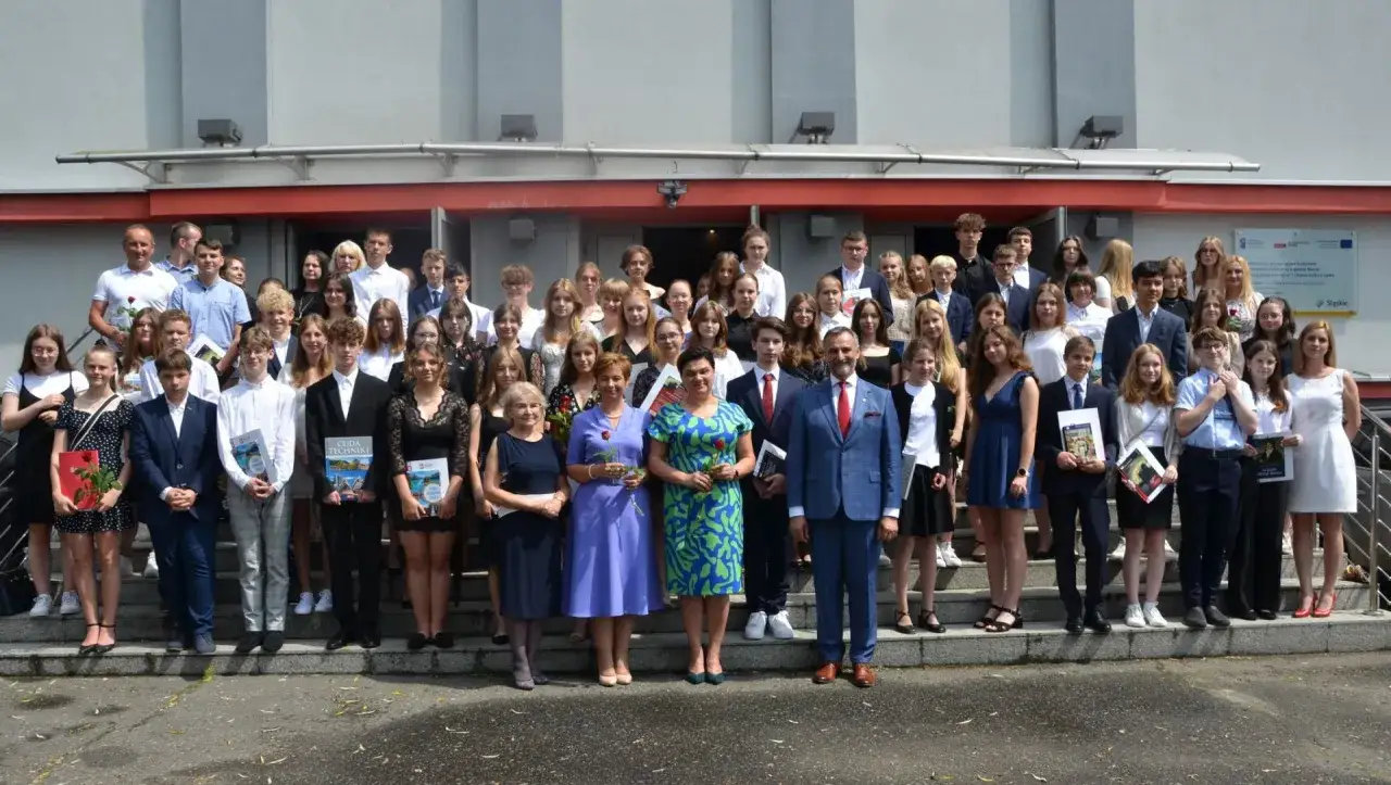 Uczniowie i nauczyciele pozują do zdjęcia po zakończeniu roku szkolnego. W rękach trzymają dyplomy i książki, a na twarzach maluje się radość. To idealny moment na piękne cytaty na zakończenie szkoły.